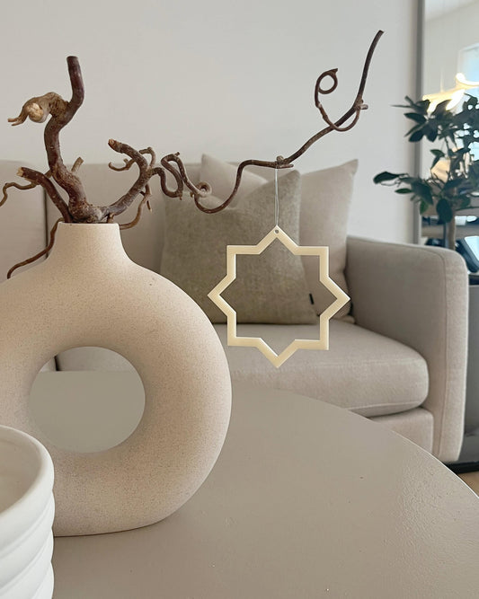 Minimalistisk stjerne i beige som hængende dekoration ved vase i stuen